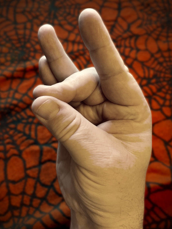 Image of hand with the thumb and middle finger touching together, and the remaining fingers held straight out. There is an orange and black spiderweb cloth in the background.